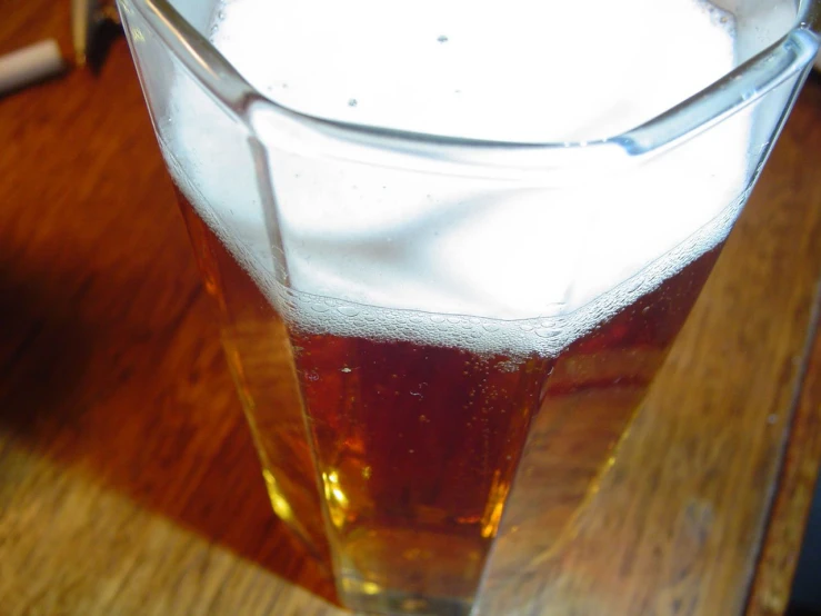 glass of beer on wooden table, with white foam