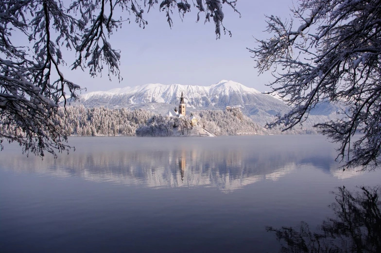a lake with a church sitting on it and snow covered mountains in the background