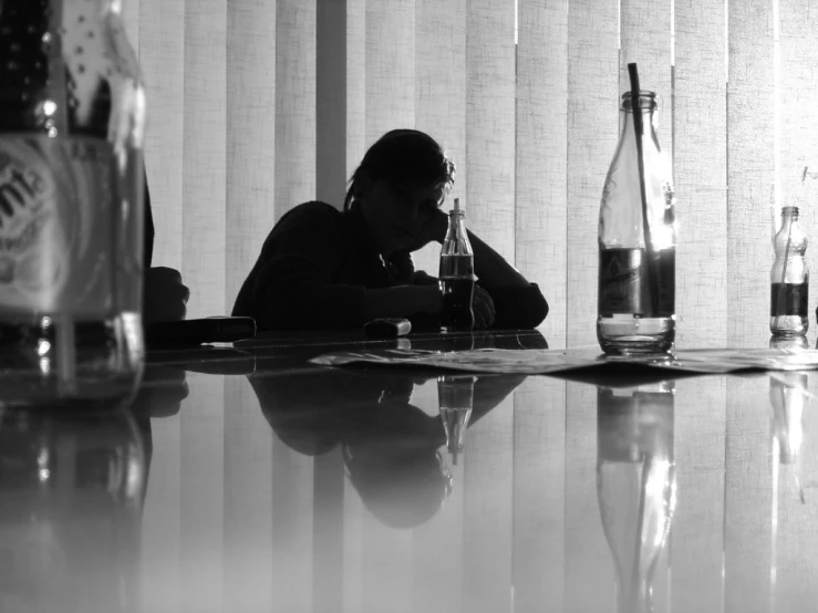 a man sitting at a table drinking soing in front of bottles