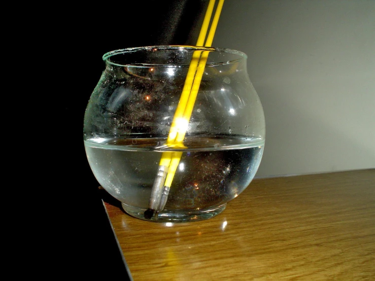 a glass filled with water and two yellow sticks inside