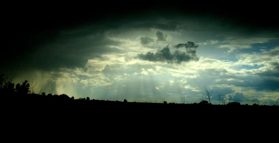 a cloudy sky over some trees with the sun peeking through