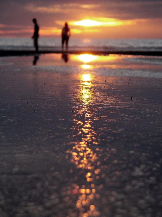 two people walking on a beach at sunset