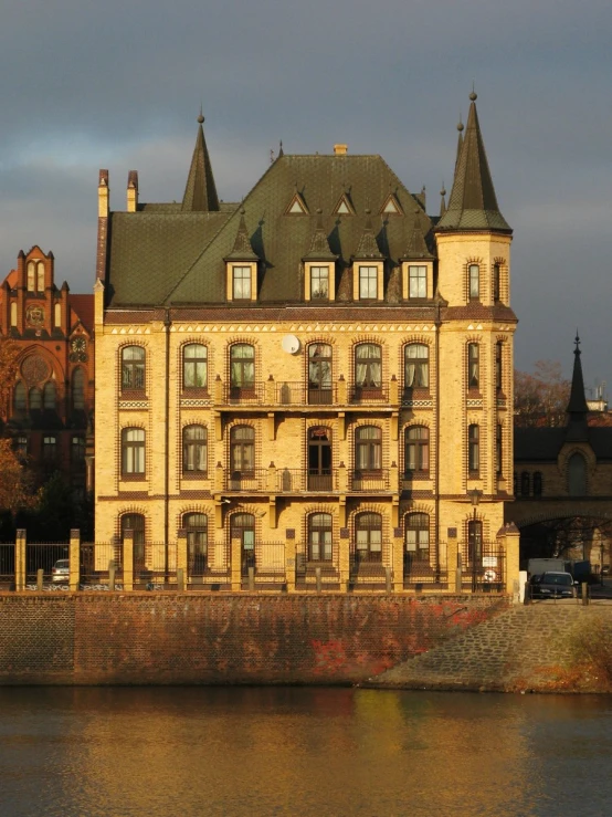 a large tan building with black roofs on top near a river