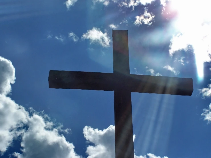 the sun beams through a cloud cover sky behind a wooden cross