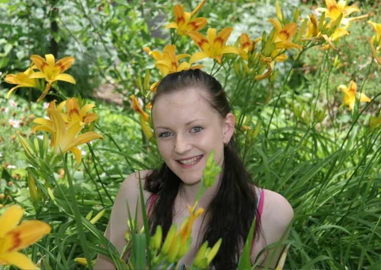 a girl with blue eyes smiling while standing amongst flowers