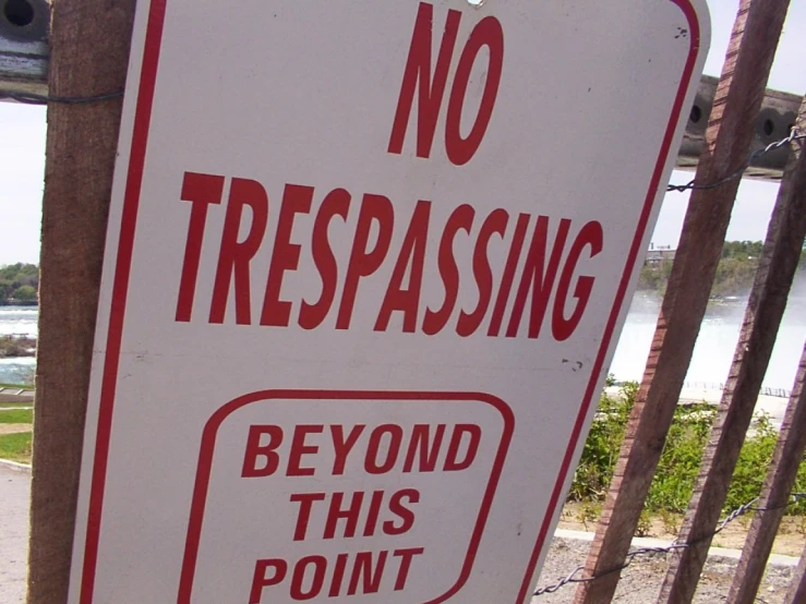 a no trespassing sign stands on a fence next to the ocean
