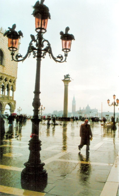 a person walking in a wet sidewalk beside some street lights