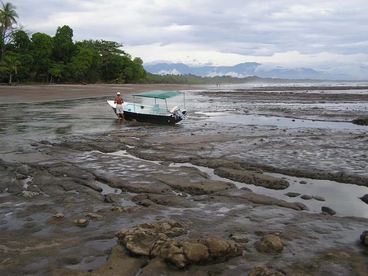 boat tied to shore with man standing next to it in low tide