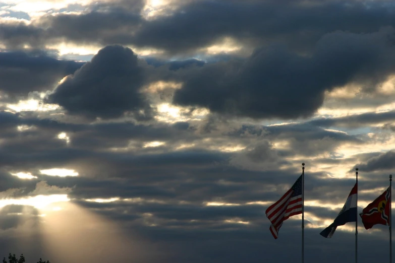 some flags are flying in the sky with the sun peeking through the clouds