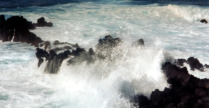 a big wave splashes over the rocks and into the water