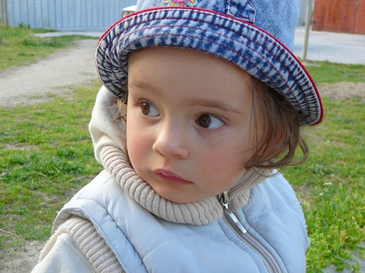young child with hat outside in yard on grass