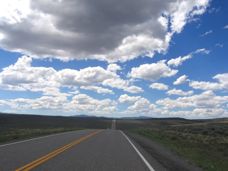 a very wide road with some tall grass and clouds