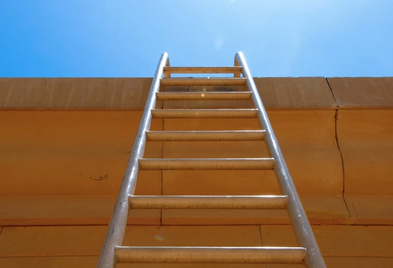 a ladder leaning against a wall against a bright blue sky