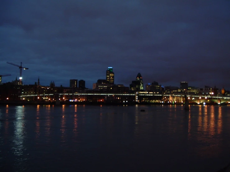 the city is lit up as the moon rises over the water