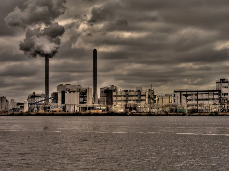 smokestacks rise from three industrial buildings overlooking a body of water