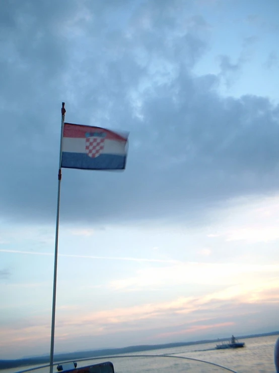 a flag flying on top of a boat next to the water