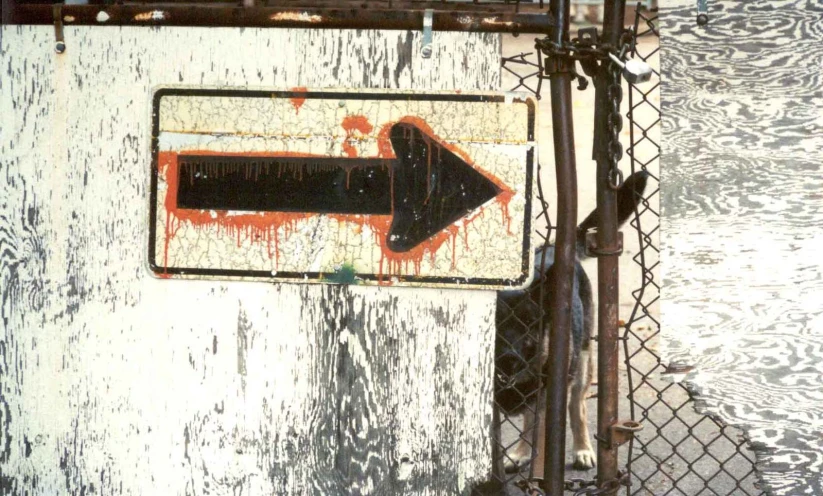 a black and orange sign on a fence and behind it is an arrow