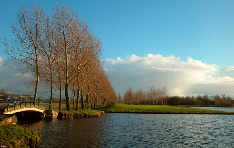 bridge over water with trees, grass and cloudy sky in background