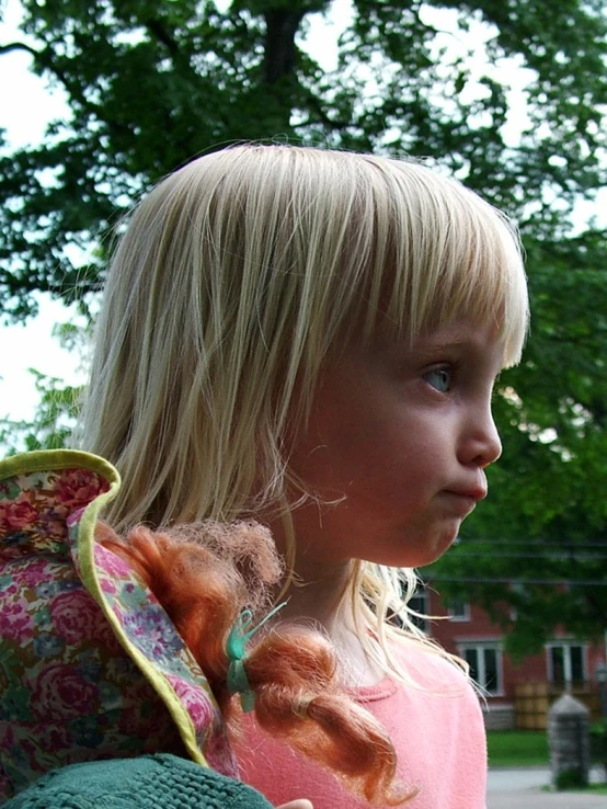 a small blonde girl carrying her doll outside