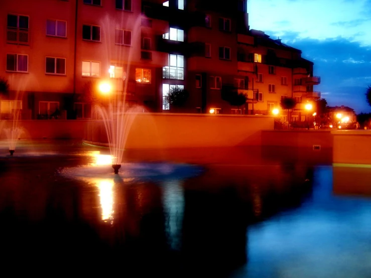 an empty water fountain surrounded by buildings with a light show in the back