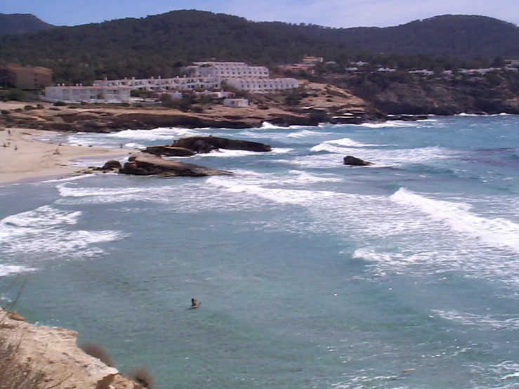 a person on a surfboard stands in the ocean near rocky beach