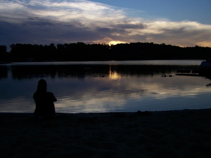 a woman sitting on the shore watching the sun set