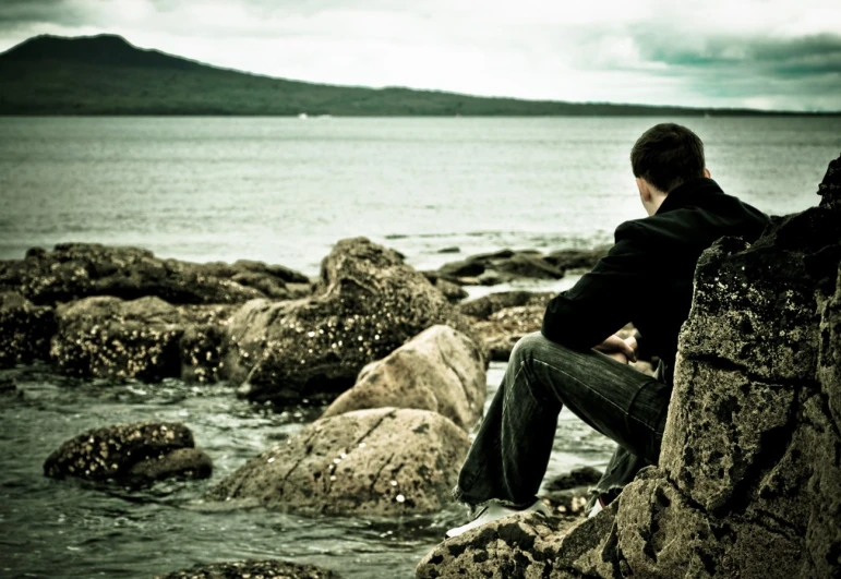 man sitting on some rocks by the water