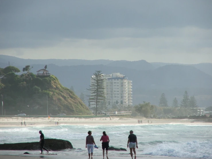 three people are standing on a beach as waves roll by