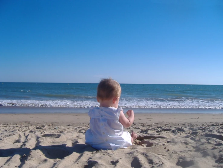 there is a little baby that is sitting on the sand