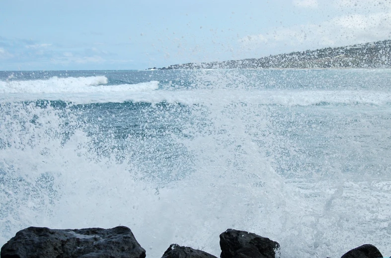 a wave crashes over the rocks on a rocky shoreline