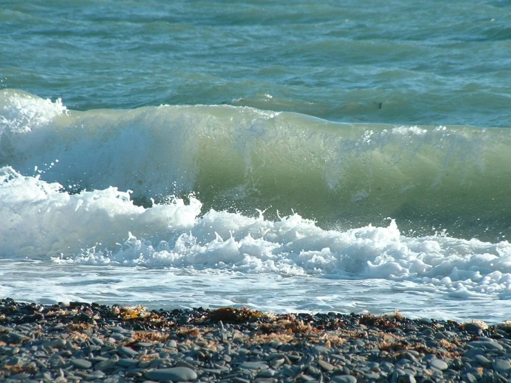 the view from the shore of the ocean of waves crashing on a pebble beach