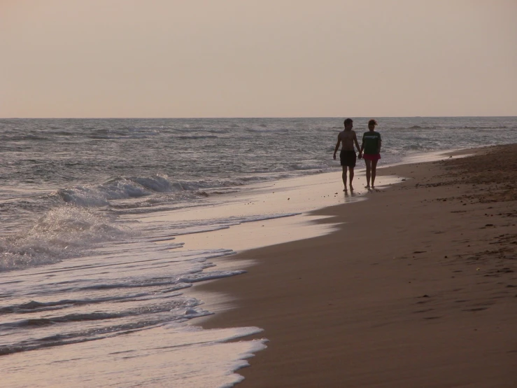 two people walking down the beach towards the ocean