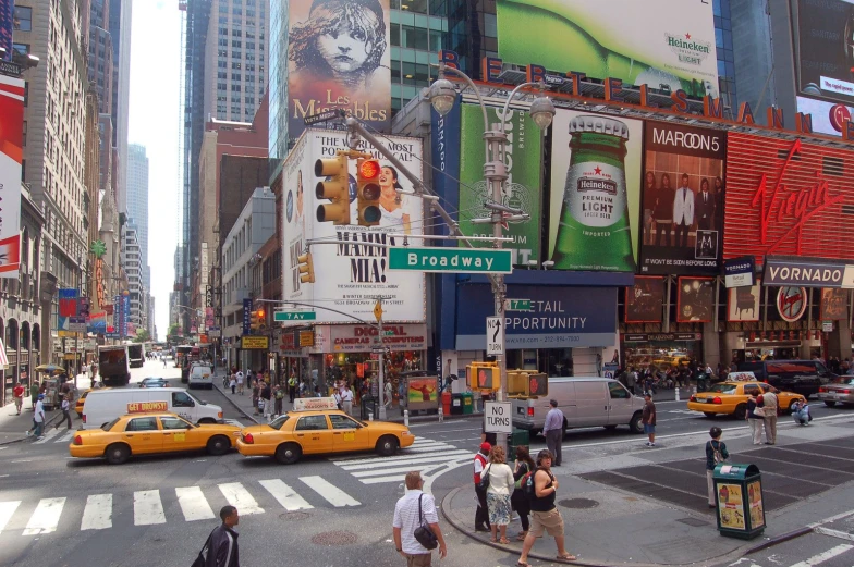 people crossing the street in times square with many tall buildings