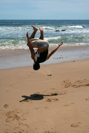 a man doing a handstand in the sand near a beach