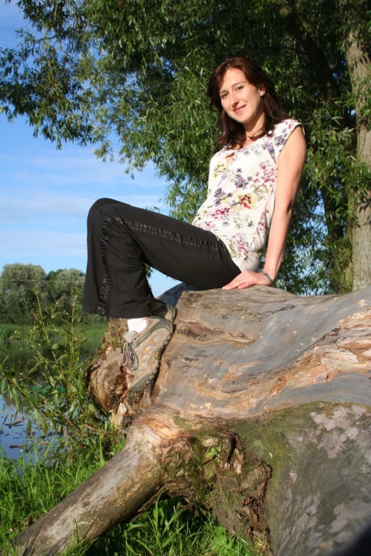 a woman sitting on a fallen tree by a lake