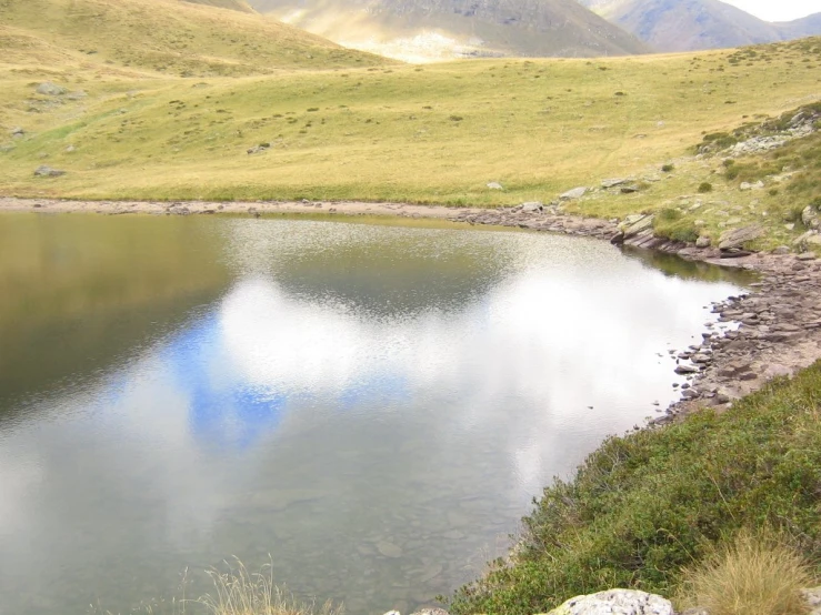a mountain lake with grass, rocks and sky in the background