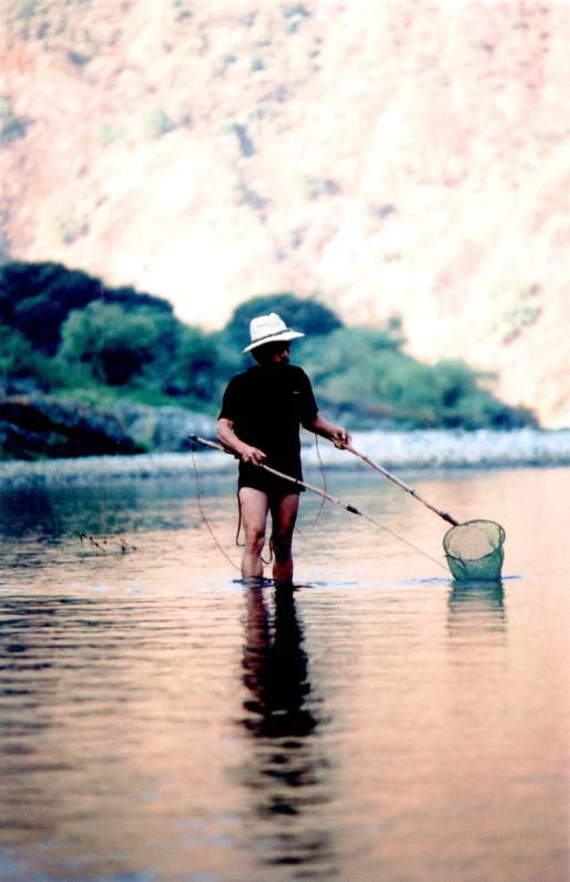 a man wading in the shallows pulling his net