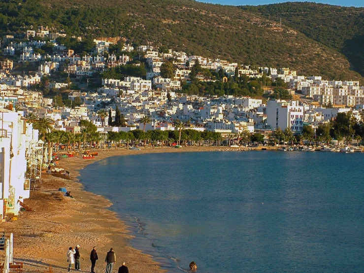 people stand on the beach in front of a city with water