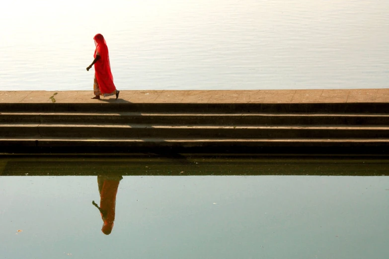 a woman in red walking down stairs near water