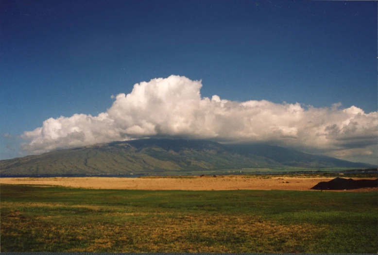 a large cloud is on a mountain with a field in the foreground