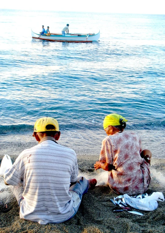 two people sitting on the beach facing the water