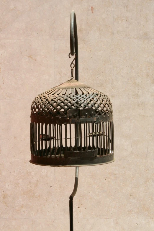 an old bird cage hanging from a metal pole