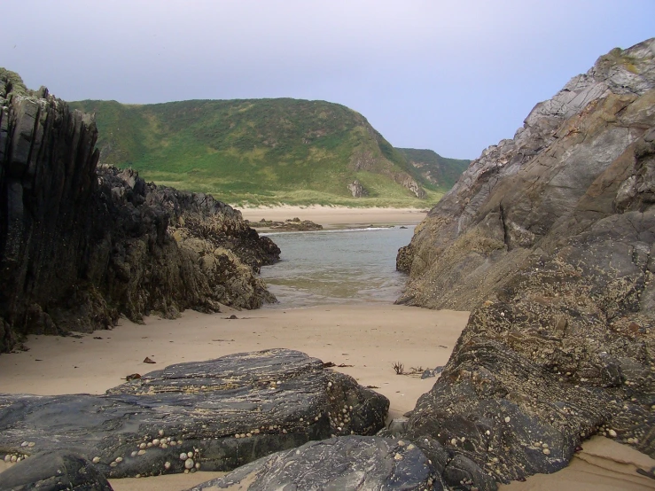 some rocks on the beach and green mountains in the distance