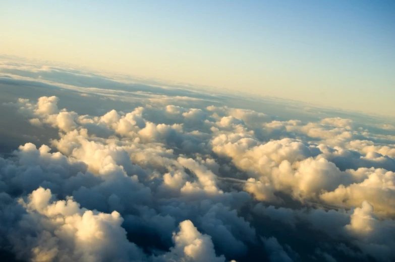 a group of clouds above the ground with a plane wing