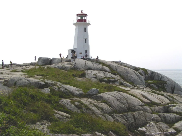 a very tall white and red light house on top of a rocky hill