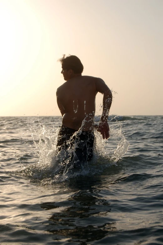 man standing in the water with sun in the background