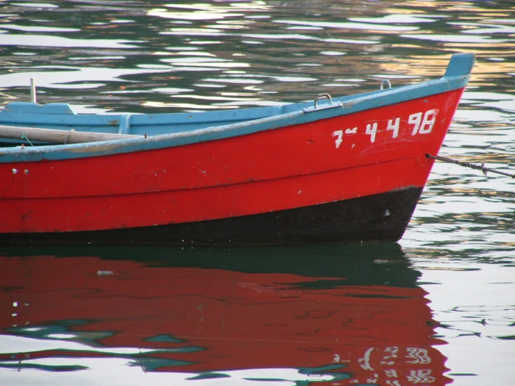 a red boat with a blue front sitting on a lake