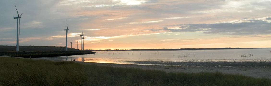 some wind mills are standing by the water