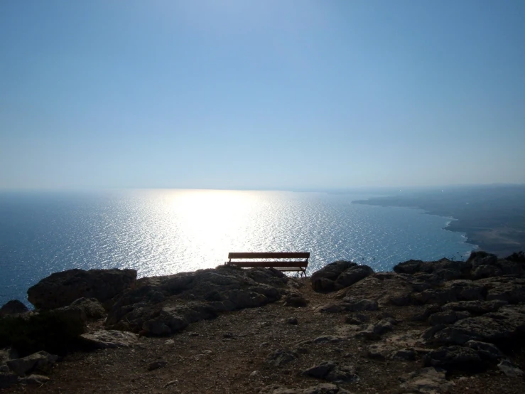 there is a bench near the ocean and blue sky