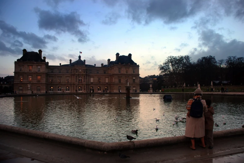 two people are standing by a lake in front of a building